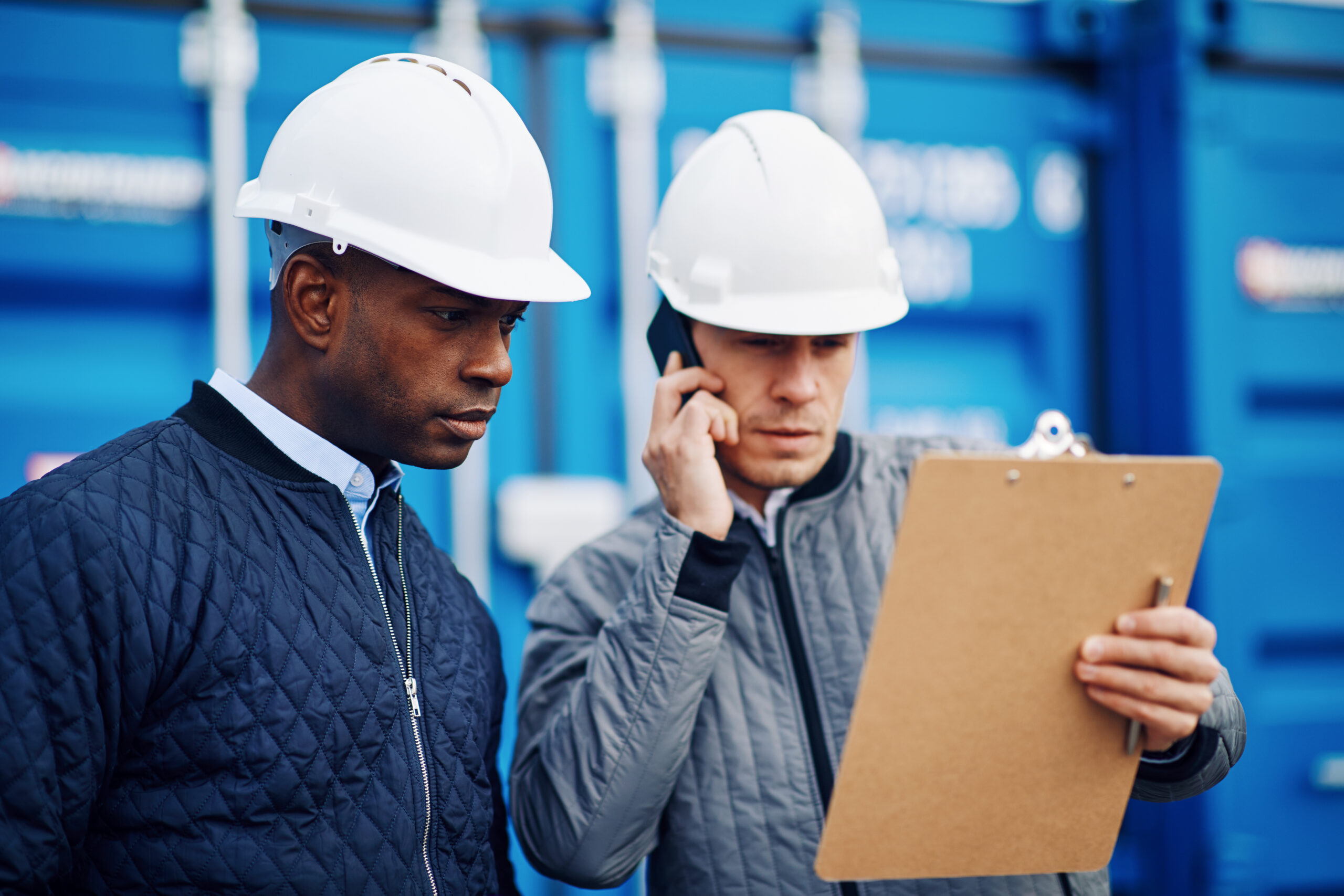 Two men in hard hats managing orders through phone conversations.