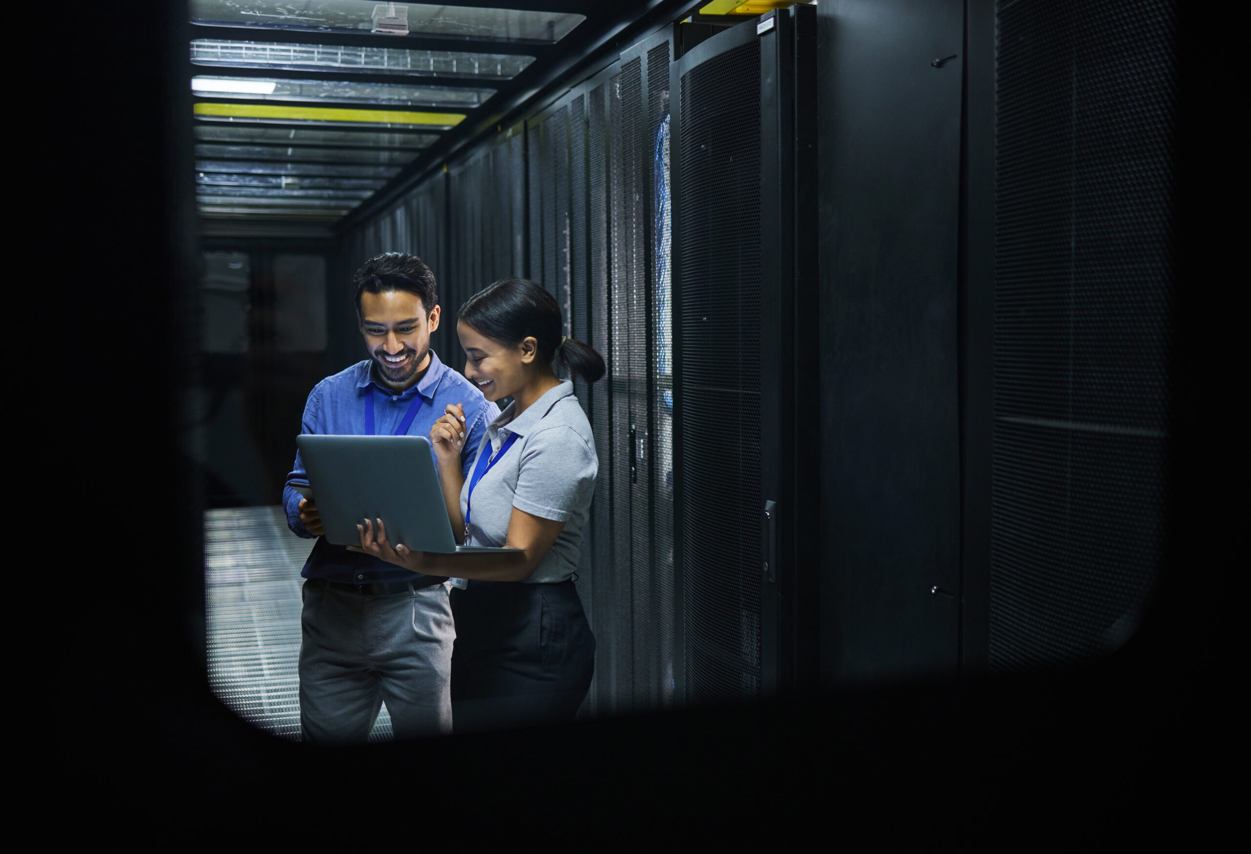 Two people in a server room integrating inventory management software with other systems, focused on a laptop.