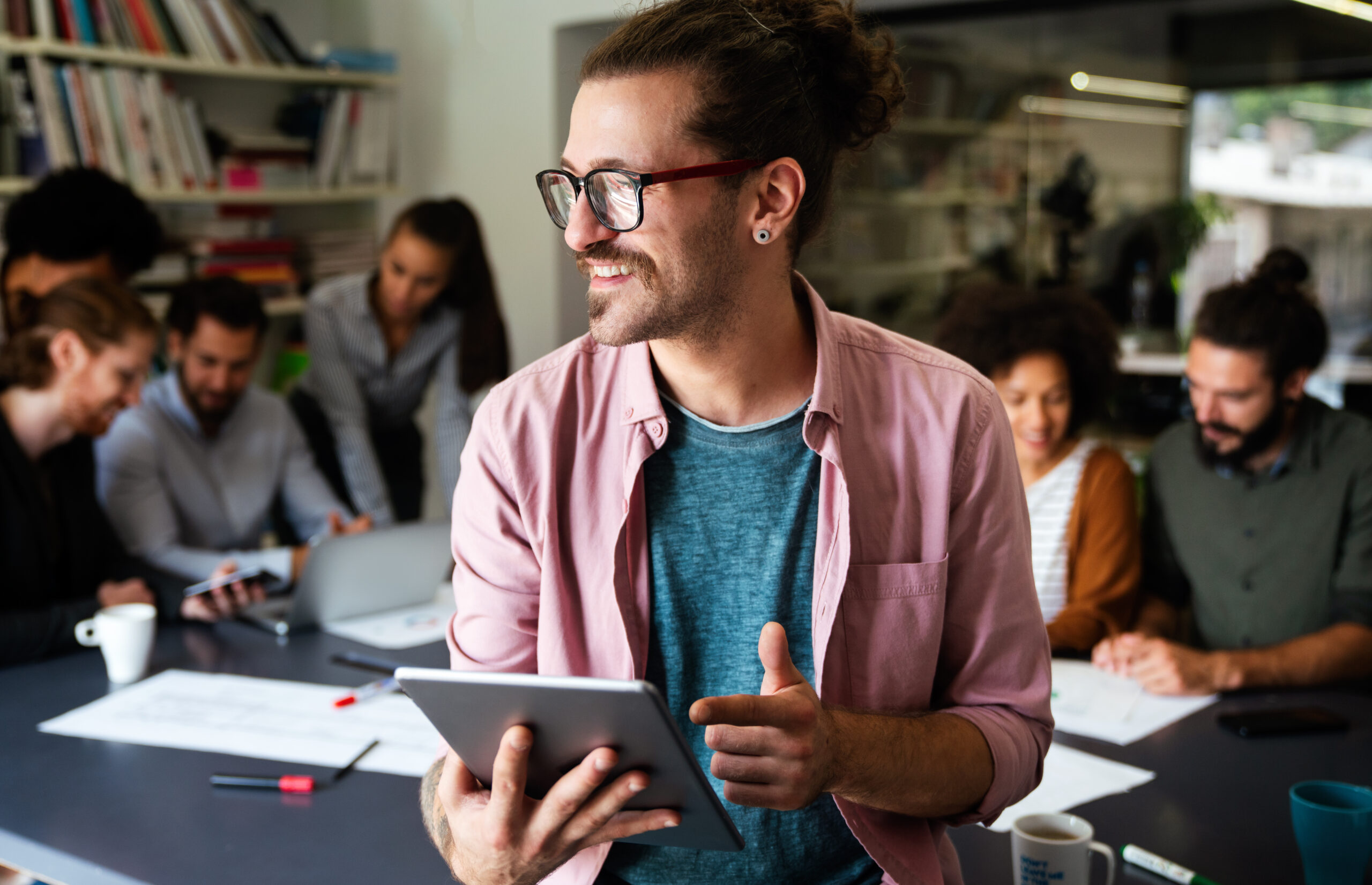 A man in glasses is using HR management software on his tablet in front of a group of people.